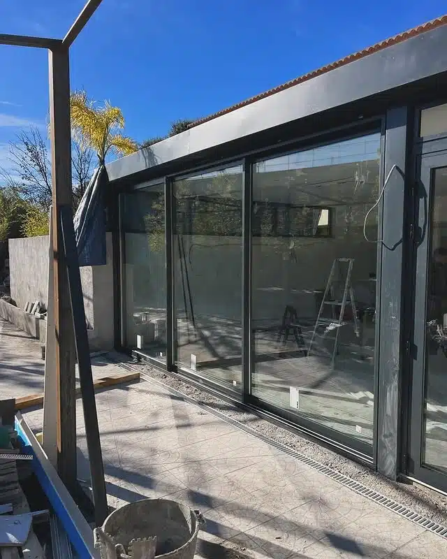 Baie vitrée coulissante en aluminium gris installée sur une terrasse moderne ensoleillée en chantier.