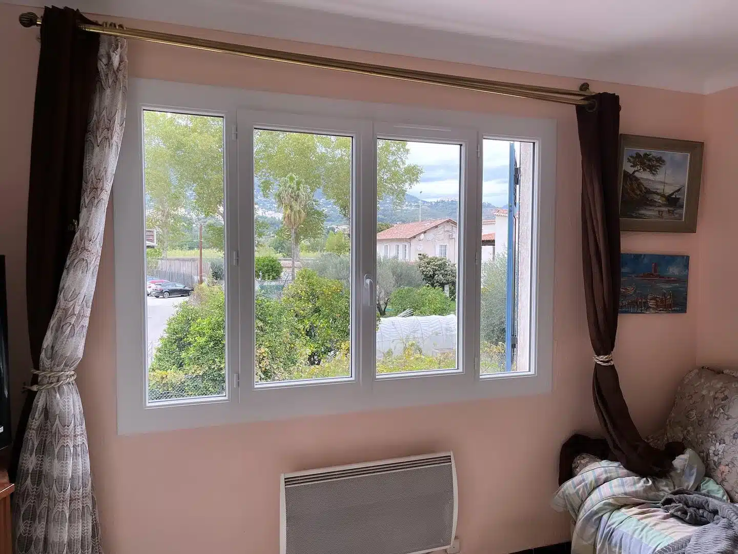 Fenêtre blanche à quatre battants avec rideaux marron ouvrant sur un jardin verdoyant dans un salon rose.